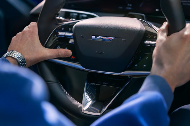 Close-up of a Man About to Press the V-Button on the 2026 OPTIQ-V Steering Wheel | Vaughn Automotive - Cadillac of Ottumwa in OTTUMWA IA